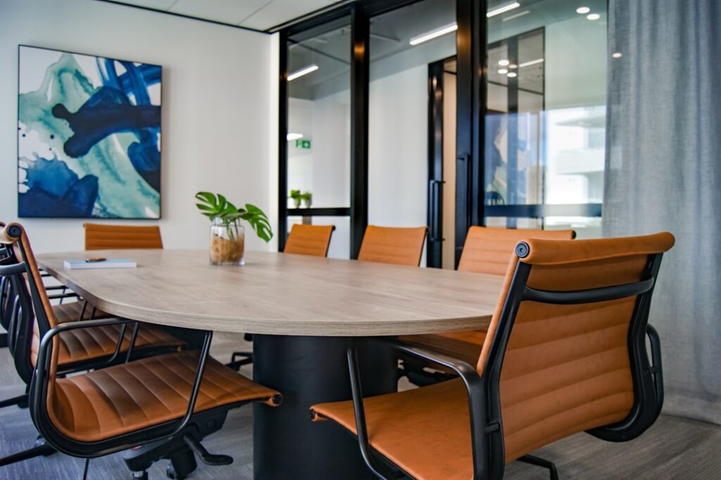 A modern conference room with an oval table and orange chairs, featuring a plant and abstract wall art.