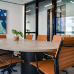A modern conference room with an oval table and orange chairs, featuring a plant and abstract wall art.