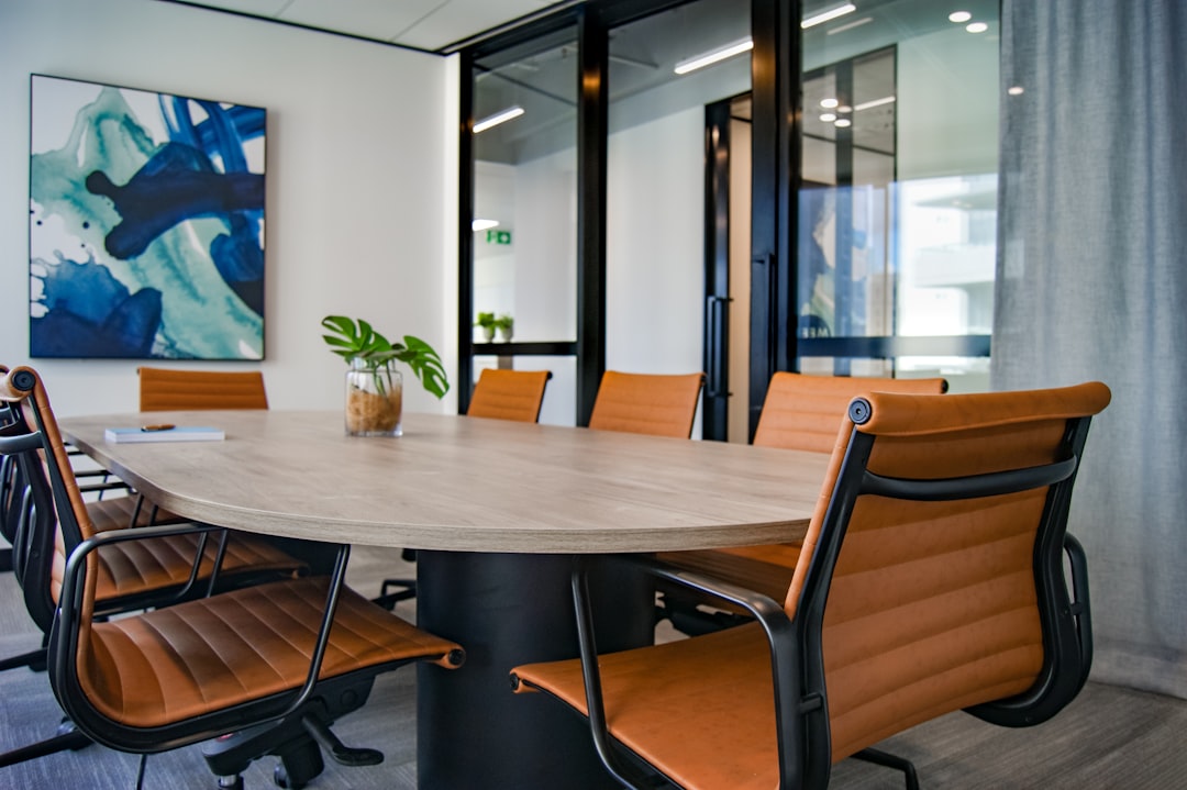 A modern conference room with an oval table and orange chairs, featuring a plant and abstract wall art.